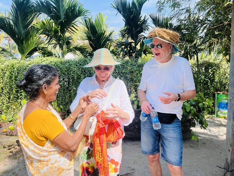 A local craftswoman showing two guests how coconut coir fibre is twisted by hand, everyone laughing together